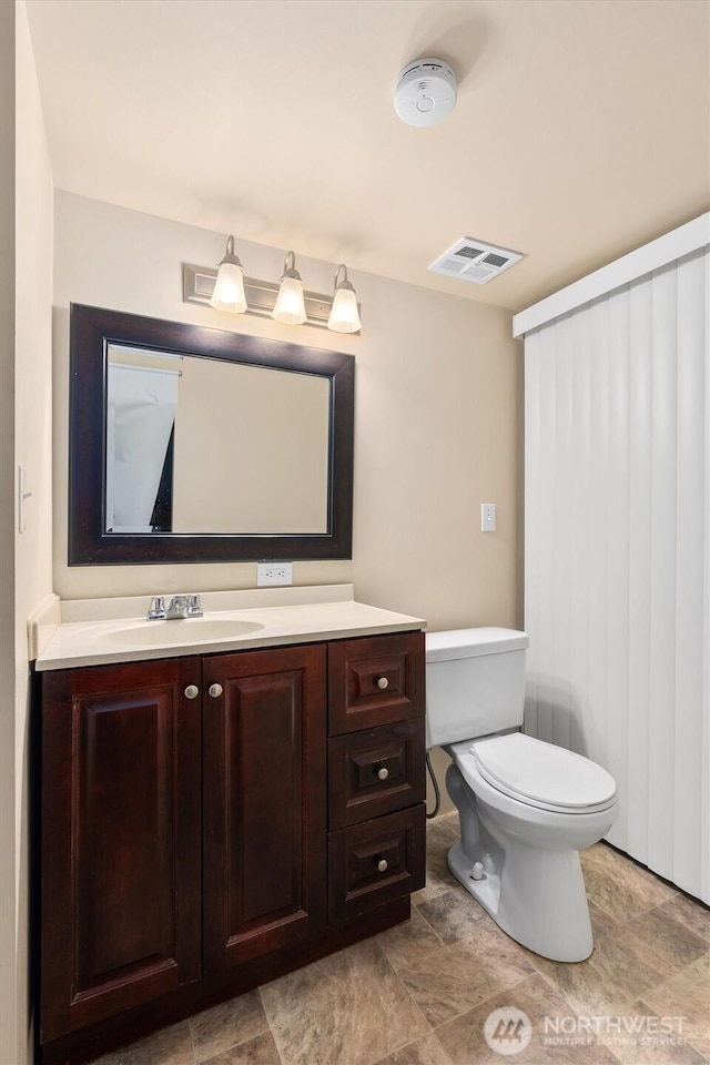 half bathroom with vanity, toilet, and visible vents