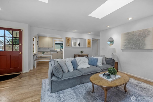 living room featuring a healthy amount of sunlight, light wood finished floors, and a skylight