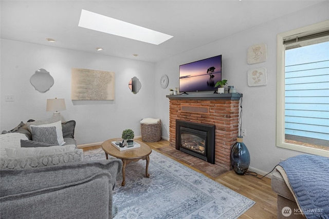 living room featuring a skylight, a fireplace, baseboards, and wood finished floors