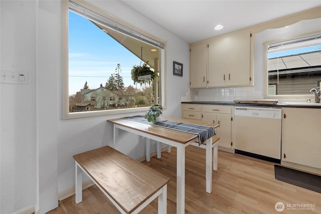 kitchen with light wood-type flooring, tasteful backsplash, white dishwasher, and a sink