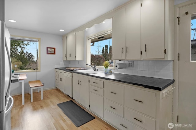 kitchen featuring decorative backsplash, freestanding refrigerator, white dishwasher, and a sink