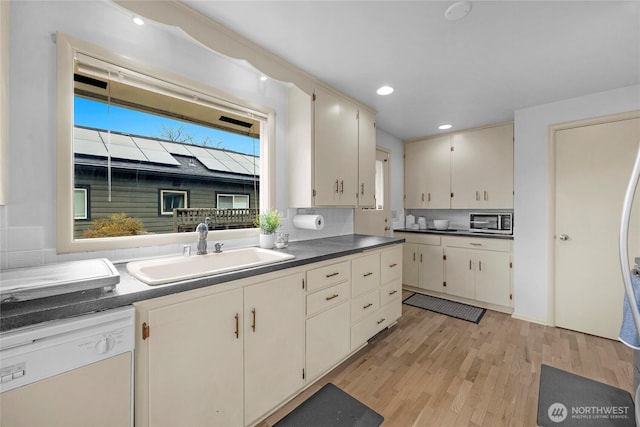 kitchen with a sink, dark countertops, light wood-style floors, and dishwasher