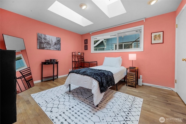 bedroom with light wood-style floors, a skylight, and baseboards