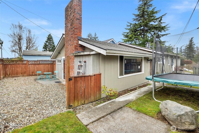 view of home's exterior featuring a patio, fence, roof with shingles, a trampoline, and a chimney