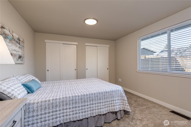 bedroom featuring multiple closets, baseboards, visible vents, and carpet flooring