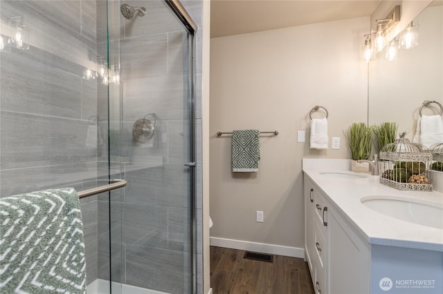 bathroom featuring a sink, wood finished floors, baseboards, a shower stall, and double vanity