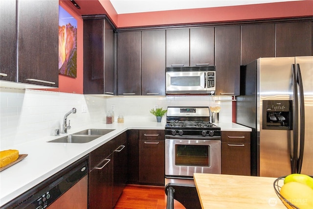 kitchen featuring appliances with stainless steel finishes, a sink, light countertops, dark brown cabinets, and backsplash