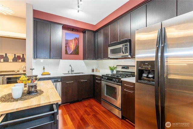 kitchen featuring dark wood-style floors, decorative backsplash, appliances with stainless steel finishes, a sink, and butcher block countertops