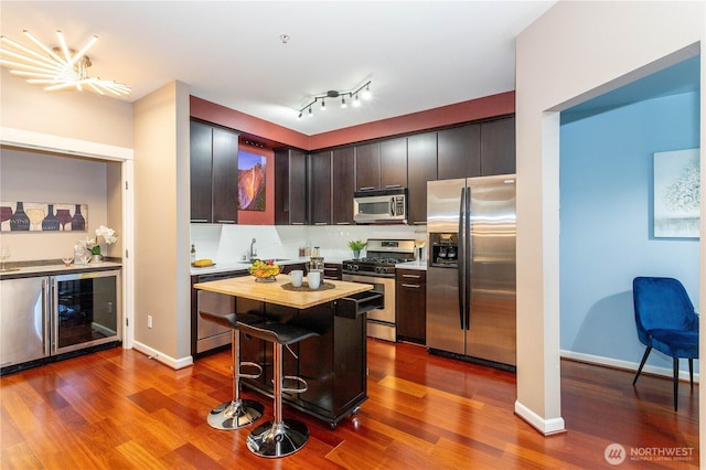 kitchen featuring a kitchen bar, wine cooler, appliances with stainless steel finishes, and dark wood-style flooring