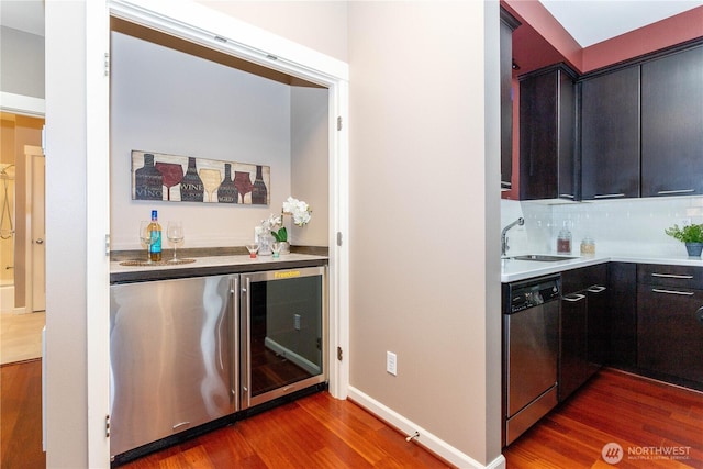 kitchen with baseboards, dishwasher, backsplash, wood finished floors, and a sink