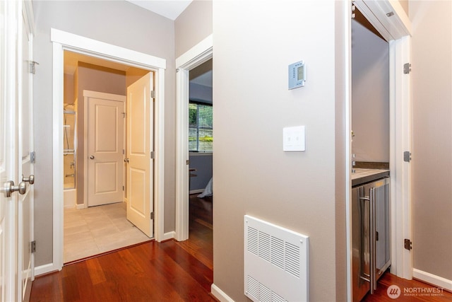 corridor featuring baseboards, wood finished floors, and heating unit