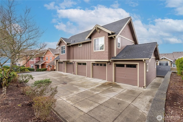 view of side of property with roof with shingles, concrete driveway, an attached garage, board and batten siding, and a residential view