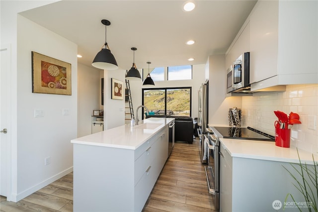 kitchen with light wood-style flooring, appliances with stainless steel finishes, a sink, light countertops, and backsplash