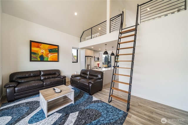 living area with recessed lighting, a towering ceiling, light wood-type flooring, baseboards, and stairs