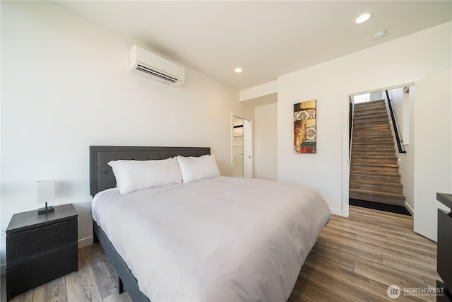 bedroom featuring baseboards, a wall unit AC, wood finished floors, and recessed lighting