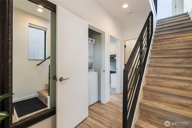 hallway featuring baseboards, stacked washer / drying machine, stairs, light wood-style floors, and recessed lighting