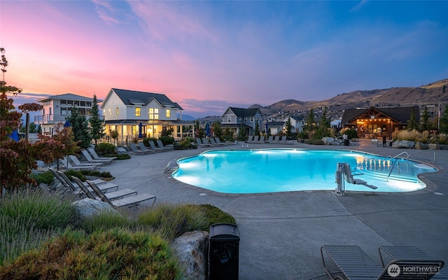 pool at dusk with a community pool, a mountain view, fence, and a patio