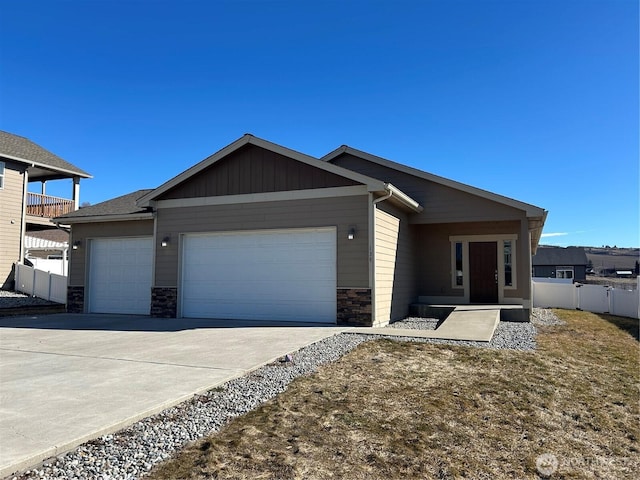 view of front of house featuring driveway, stone siding, an attached garage, fence, and board and batten siding