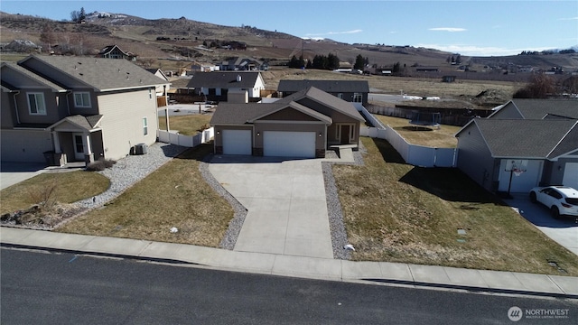 view of front facade with a mountain view, a garage, fence, driveway, and a residential view