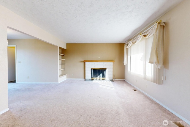 unfurnished living room featuring baseboards, carpet, a textured ceiling, a brick fireplace, and built in shelves