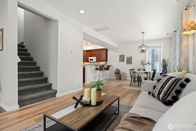 living room featuring light wood finished floors, baseboards, visible vents, stairway, and recessed lighting