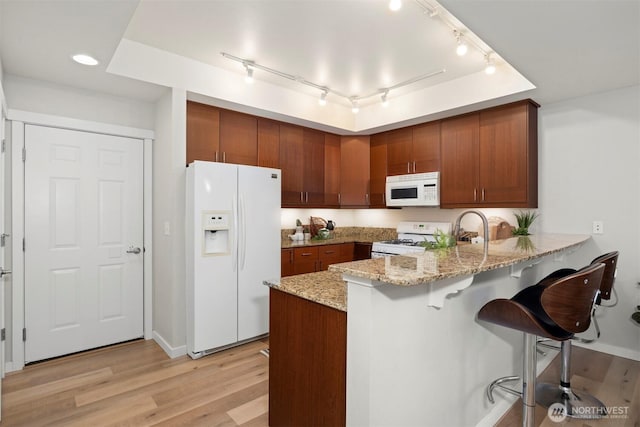 kitchen featuring light stone countertops, a peninsula, white appliances, light wood-style floors, and brown cabinets