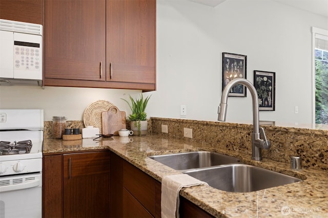 kitchen with light stone countertops, white appliances, and a sink