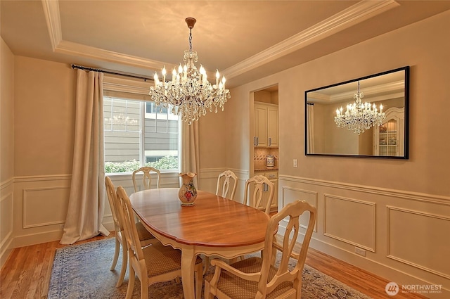 dining room featuring light wood-style floors, a chandelier, a decorative wall, and a tray ceiling