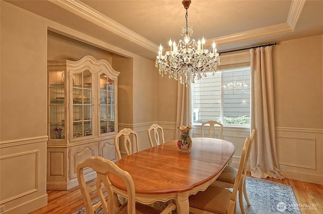 dining area with a wainscoted wall, light wood-style flooring, a tray ceiling, and ornamental molding