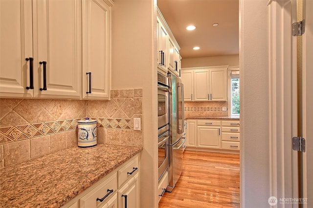 kitchen featuring light stone countertops, recessed lighting, white cabinets, light wood-type flooring, and decorative backsplash