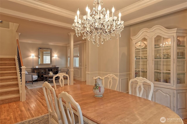 dining area featuring wood finished floors, wainscoting, crown molding, and stairs