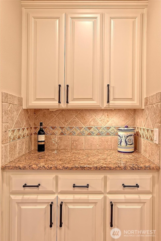 interior space with light stone counters, white cabinetry, and backsplash