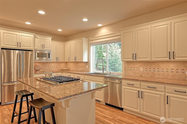 kitchen with light wood-style flooring, appliances with stainless steel finishes, light stone counters, and a sink