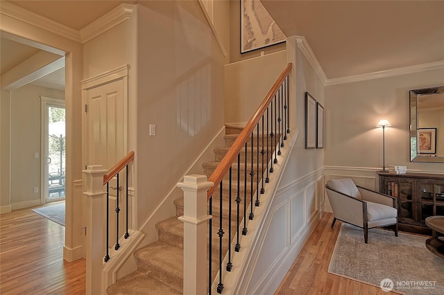 stairway featuring crown molding, a decorative wall, and wood finished floors