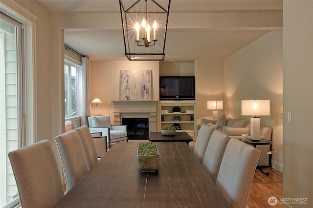 dining room featuring baseboards, a glass covered fireplace, wood finished floors, an inviting chandelier, and baseboard heating