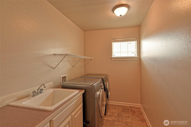 laundry room with a textured wall, a sink, baseboards, washer and dryer, and cabinet space