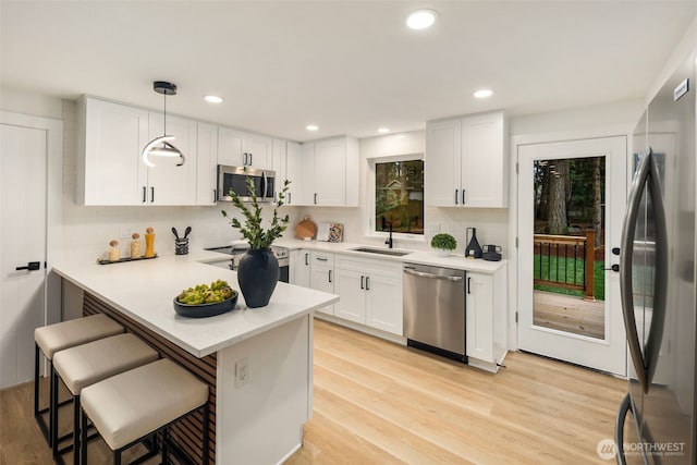 kitchen featuring a breakfast bar area, a peninsula, a sink, appliances with stainless steel finishes, and light wood-type flooring