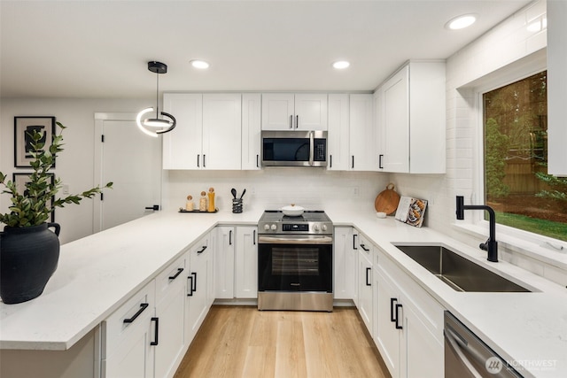 kitchen featuring light wood-style flooring, appliances with stainless steel finishes, a peninsula, white cabinetry, and a sink