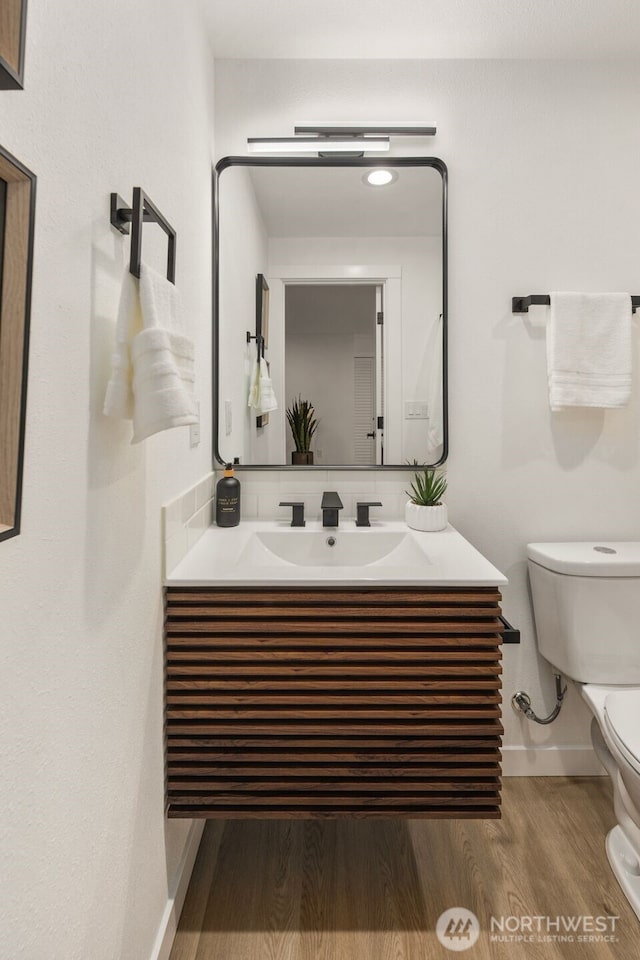 half bath with toilet, vanity, baseboards, and wood finished floors