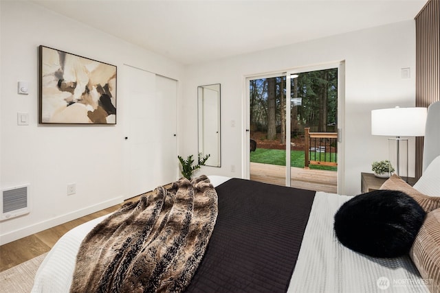 bedroom with wood finished floors, visible vents, baseboards, a closet, and access to outside