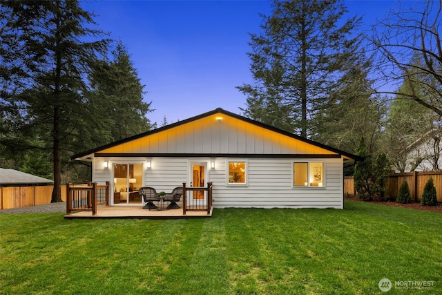 back of house at dusk with a yard, a wooden deck, and fence