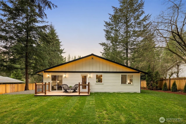 back of house at dusk featuring a wooden deck, a yard, and a fenced backyard