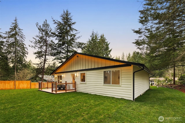 back of property at dusk with a lawn, a deck, and fence