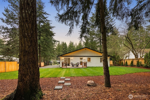 back of property at dusk featuring a patio area, a yard, fence, and board and batten siding