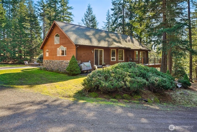 view of front facade with a shingled roof, a front yard, and stone siding