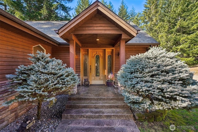 property entrance featuring covered porch and a shingled roof