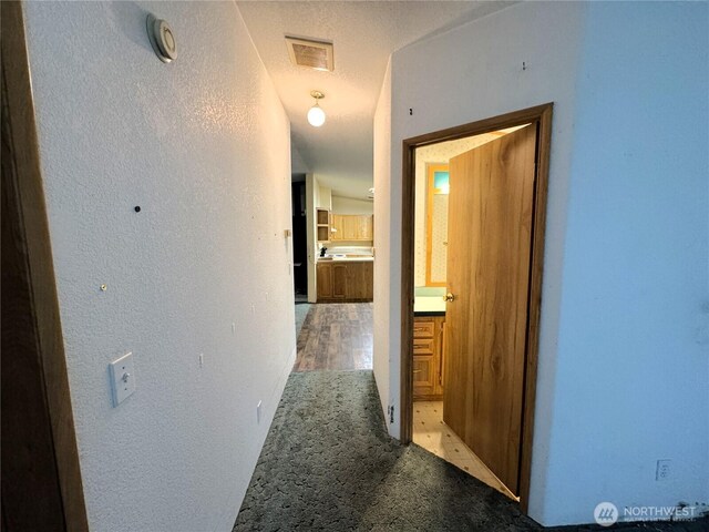 corridor featuring visible vents, a textured wall, and light colored carpet