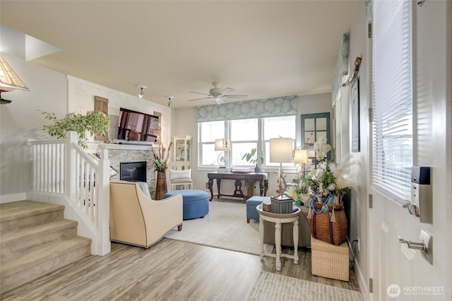 living area featuring baseboards, a ceiling fan, stairway, wood finished floors, and a stone fireplace