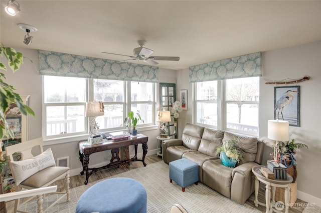 living room featuring ceiling fan, visible vents, baseboards, and wood finished floors