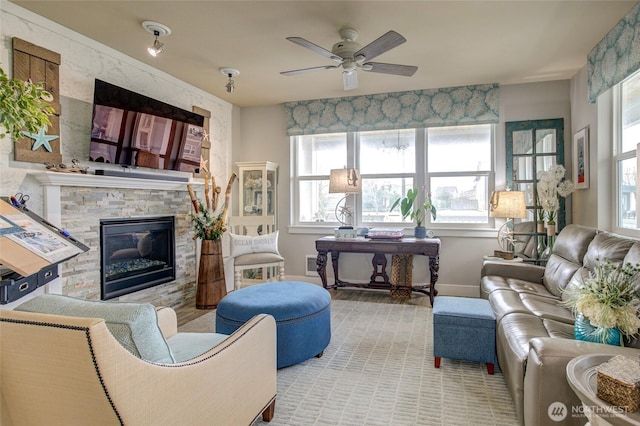 living room featuring a ceiling fan, a stone fireplace, and baseboards